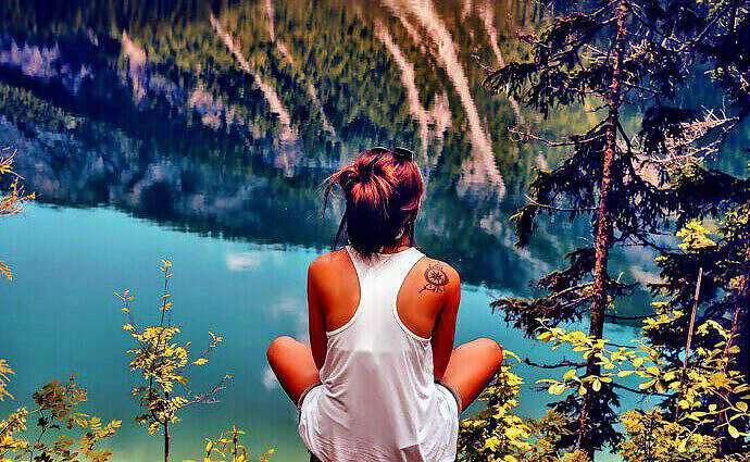 Eine junge Frau sitzt im Schneidersitz auf einem Felsvorsprung und schaut auf den Fluss unter ihr.