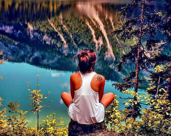 Eine junge Frau sitzt im Schneidersitz auf einem Felsvorsprung und schaut auf den Fluss unter ihr.