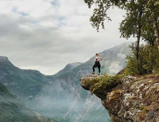 Eine junge Frau steht auf einem Felsvorsprung und schaut tief ins Tal.
