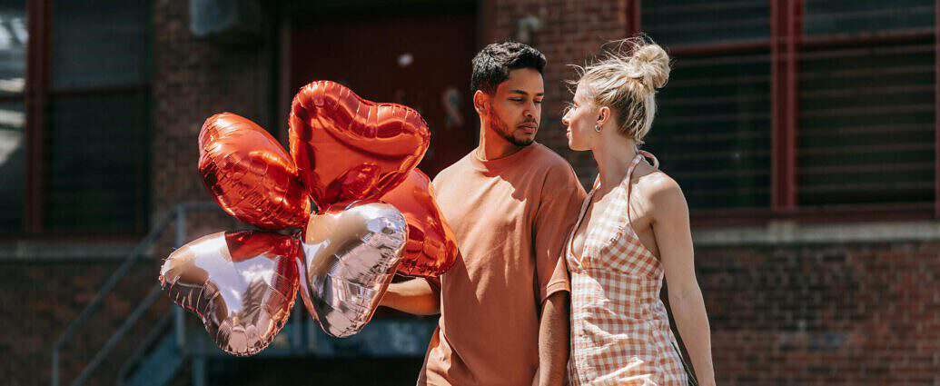 Ein Liebespaar, das sich beim Gehen anschaut und Herzluftballons in den Händen hält.