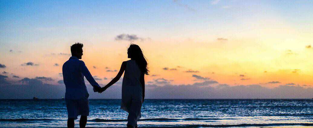 Ein verliebtes Liebespaar geht bei Sonnenuntergang Hand in Hand am Strand spazieren.