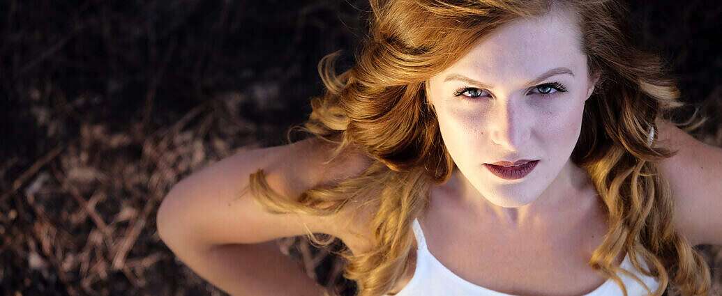 Auf dem Boden liegt eine junge Frau mit langen roten Haaren und schaut nach oben.