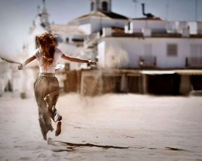 Eine junge Frau läuft im Sand und lässt Sand aus ihren Händen auf den Boden fallen.