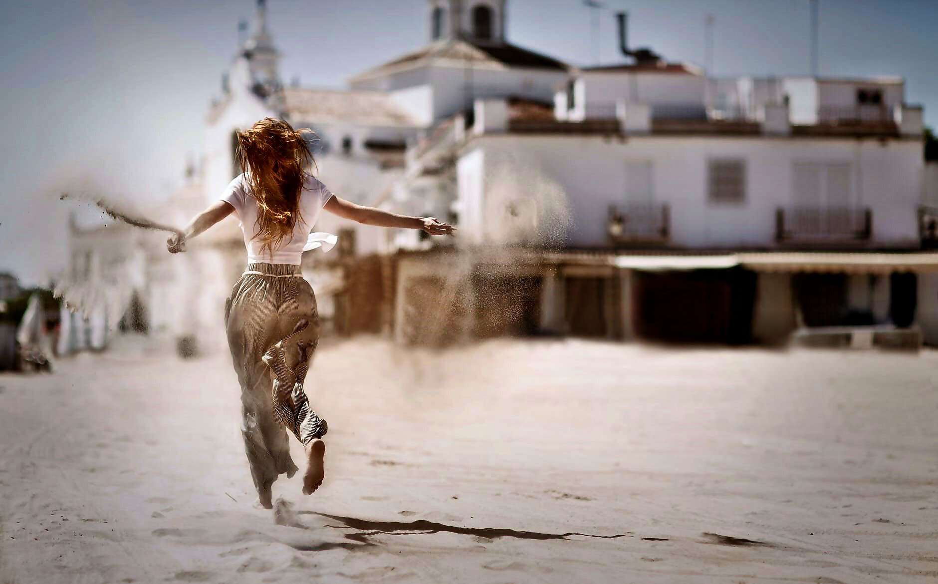 Eine junge Frau läuft im Sand und lässt Sand aus ihren Händen auf den Boden fallen.