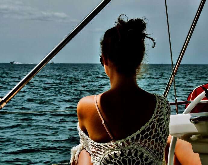 Eine junge Frau sitzt entspannt auf einem Segelboot und schaut auf das Meer.