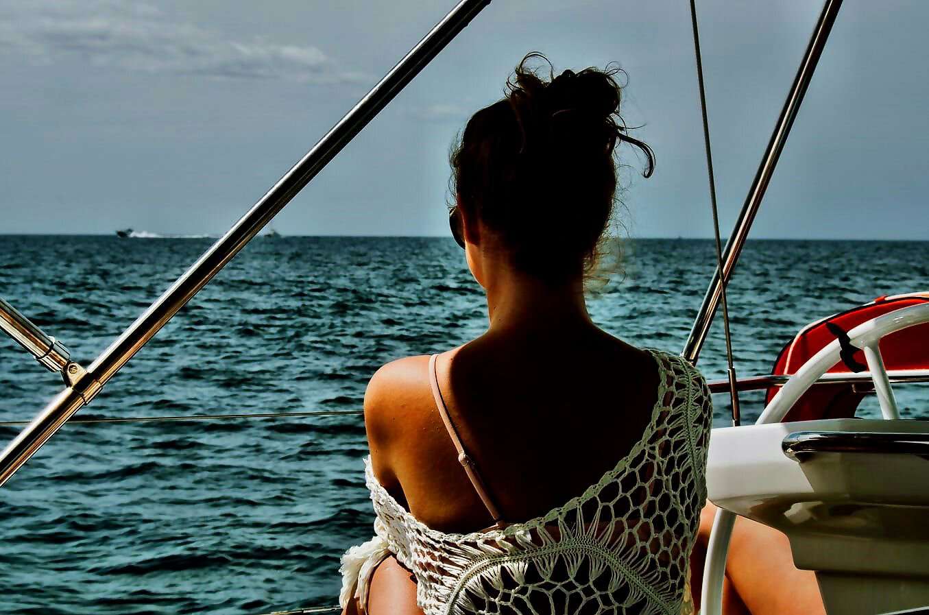 Eine junge Frau sitzt entspannt auf einem Segelboot und schaut auf das Meer.