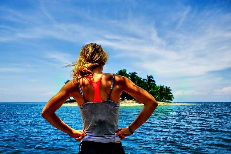 Eine junge Frau steht am Strand und schautauf einer Insel am Meer.