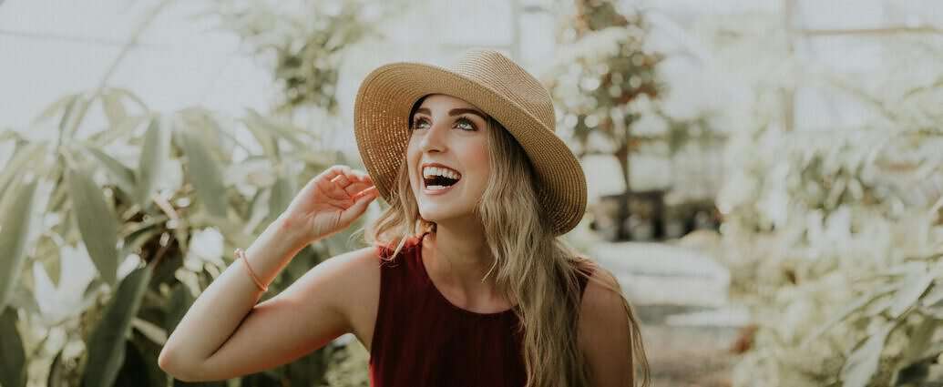 Eine junge Frau mit Hut lacht aus vollem Herzen.