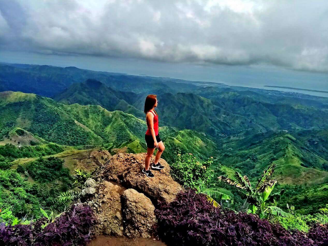 Eine junge Frau steht auf einem Berggipfel und schaut in die Ferne.