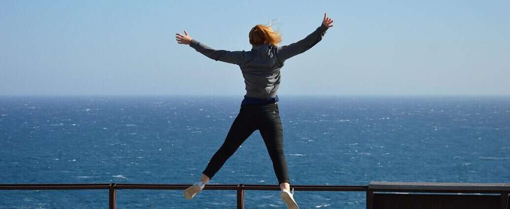 Eine junge Frau springt vor Freude in die Luft. Vor ihr ist das Meer zu sehen.