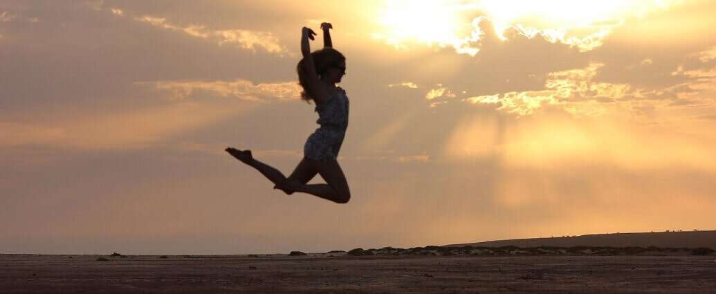 Das Bild zeigt eine junge Frau, die im Sonnenuntergang am Strand in die Luft springt.
