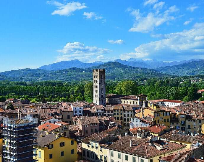 Zu sehen ist ein Stadtbild von Lucca mit seinen Gebäuden und im Hintergrund den Bergen.