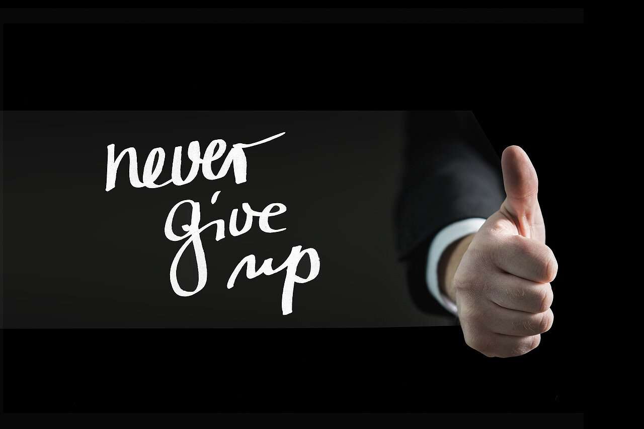 Ein Bild mit einem nach oben zeigenden Daumen und dem Schriftzug „Never give up”.