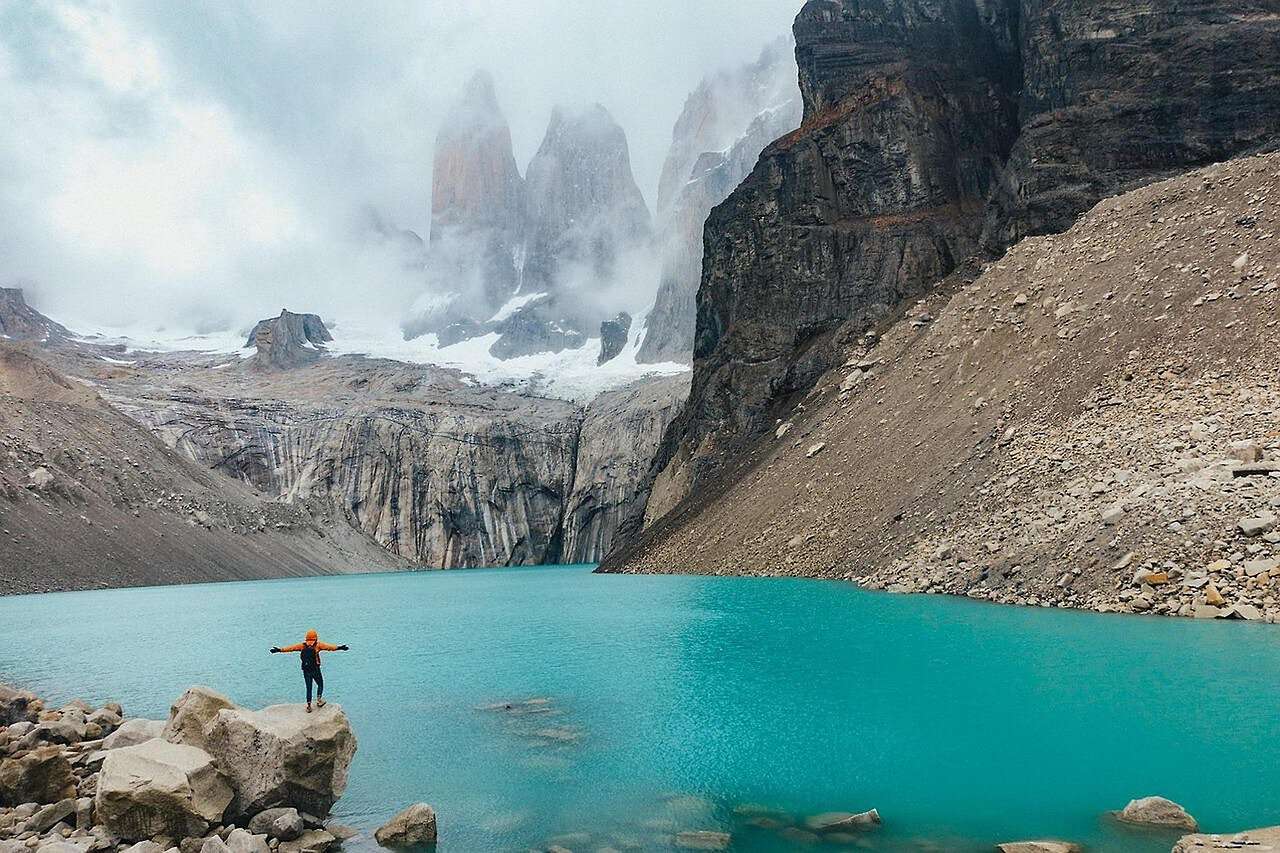 Eine junge Frau steht auf einer kleinen Klippe in Chile-Patagonien. Vor ihr erstreckt sich eine Landschaft aus Eisbergen.