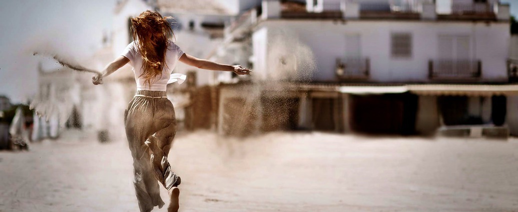 Eine junge Frau läuft vor sich hin und streut Sand aus ihren Händen auf den Boden.